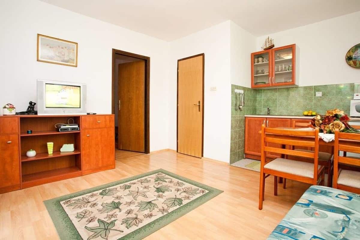 A compact kitchen with wooden cabinets, a dining table with chairs, and a small television on a shelf.