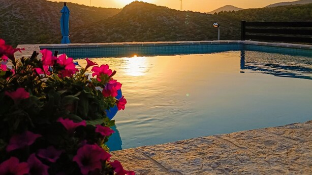 A serene pool area with a sunset view, surrounded by hills and a distant tower. - Apartments Aura (Seget)