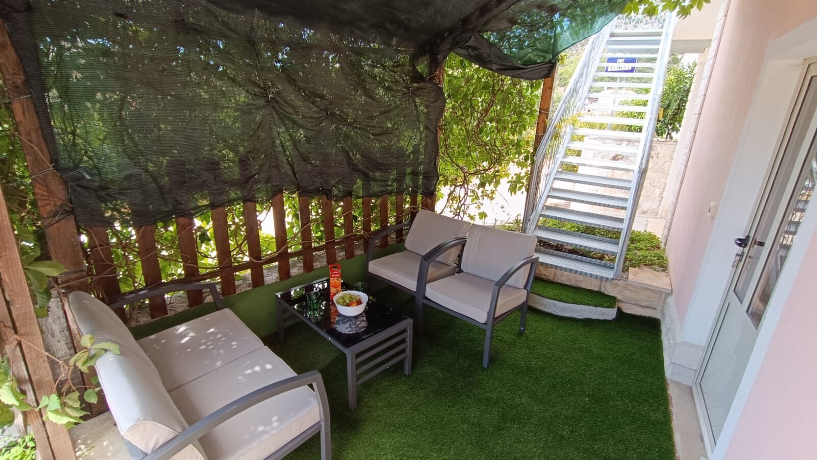 A patio with a table and two chairs, a small garden area with artificial grass, and a wooden fence.