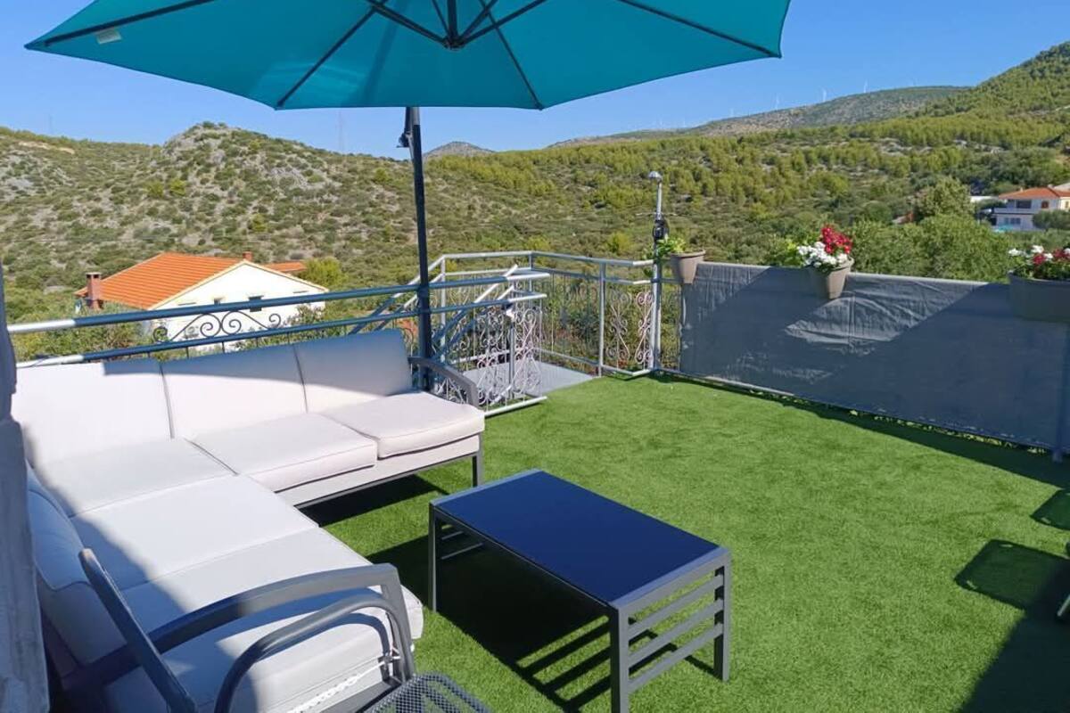 A terrace with a white sofa, a small table, and a large blue umbrella.