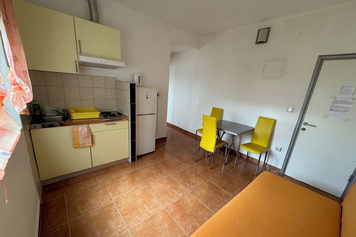 Cocina compacta con armarios amarillos, un refrigerador blanco y un comedor con dos sillas amarillas.