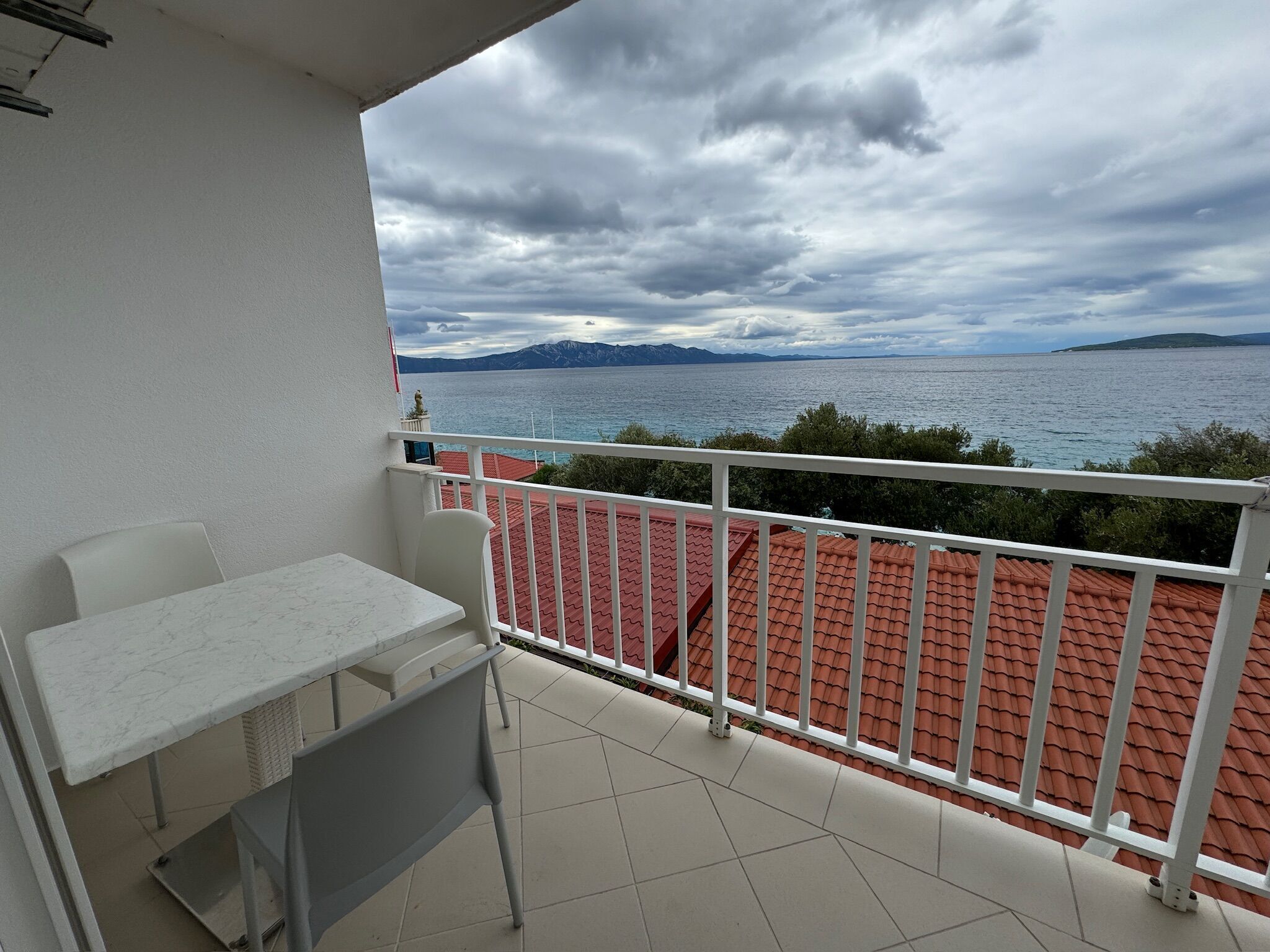 A balcony with a table and chairs, overlooking a body of water and distant mountains.