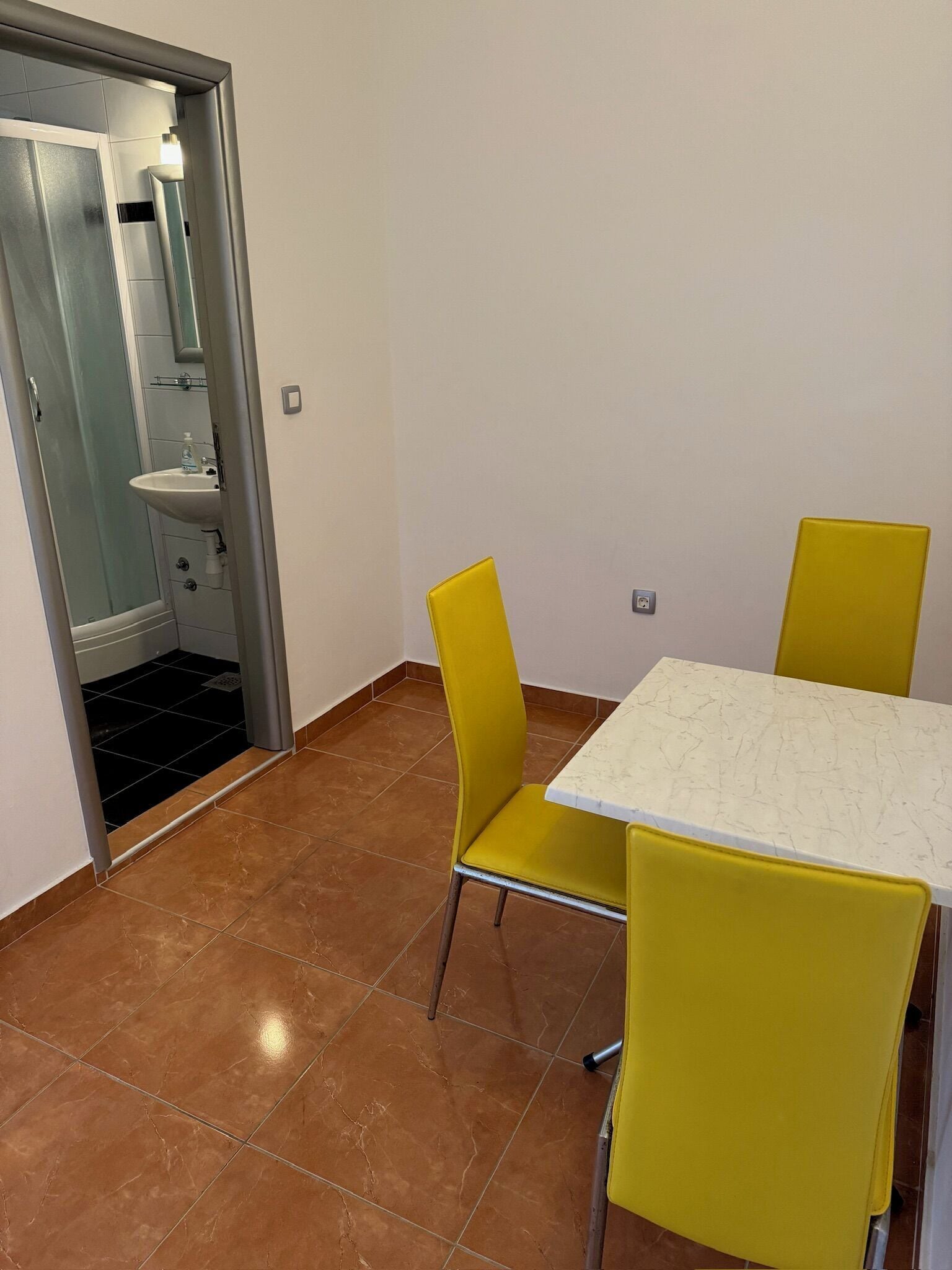 A room with a tiled floor, a white table with a marble top, and two yellow chairs.