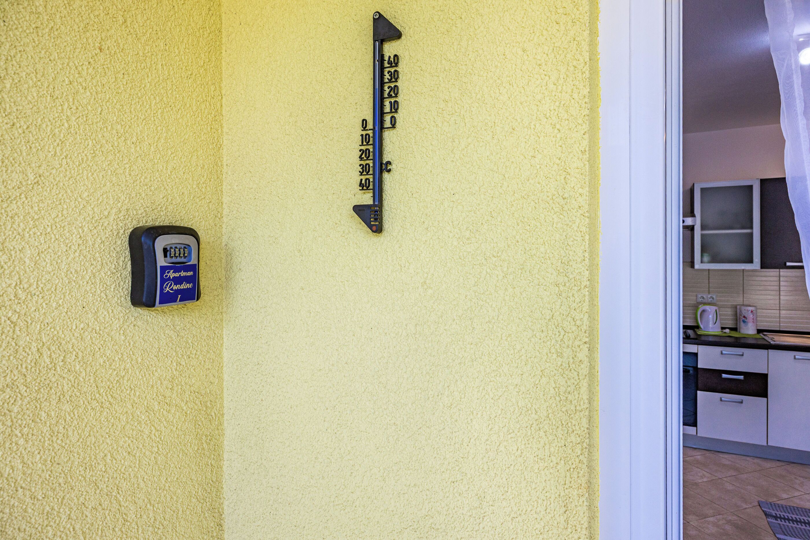 Een thermometer aan de muur en een kaartsleutel-lezer op een geel oppervlak met structuur.