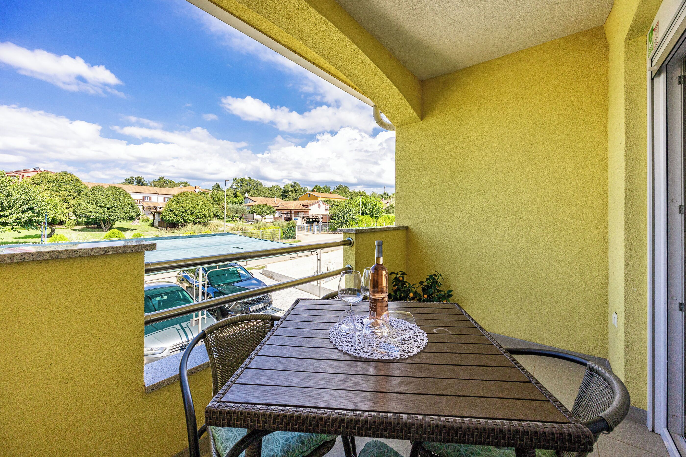 Een balkon met een tafel, stoelen, een fles en glazen.