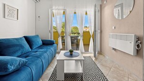A modern living room with a blue sofa, a small white table with a plant, and a patterned rug. - Apartments Rondine (Brtonigla)