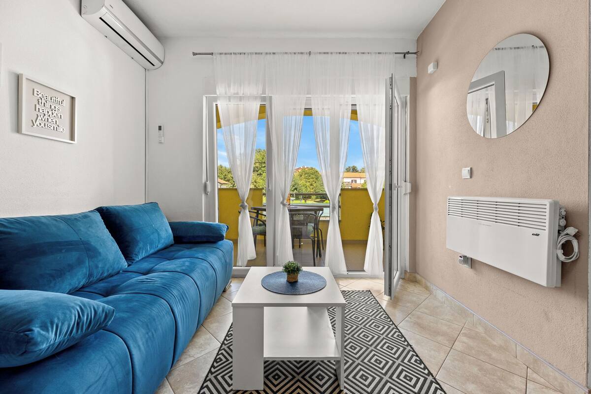 Een moderne woonkamer met een blauwe bank, een witte bijzettafeltje met een plant, en een kamerkleed met een patroon.
