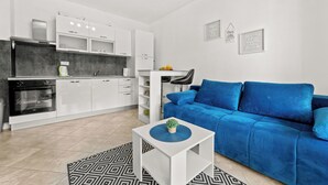 A modern kitchen with white cabinets and a blue sofa in a living area. - Apartments Rondine (Brtonigla)