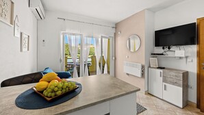 A modern kitchen with a dining area, a TV mounted on the wall, and a view of the outside. - Apartments Rondine (Brtonigla)