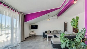 A modern living room with a grey sofa, a white coffee table, and a large potted plant. - Apartments Deepwater (Split)