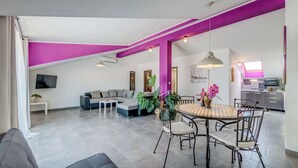 A modern living space with a dining area, a sofa, and a television. - Apartments Deepwater (Split)