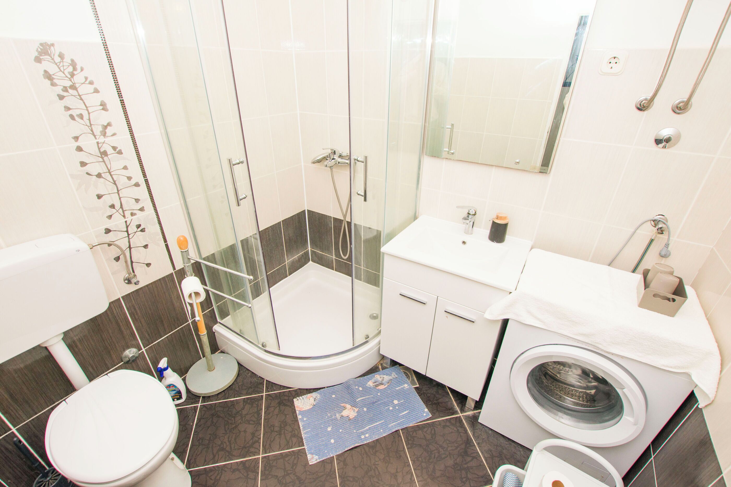 A bathroom with a glass-enclosed shower, a toilet, a sink, and a washing machine.