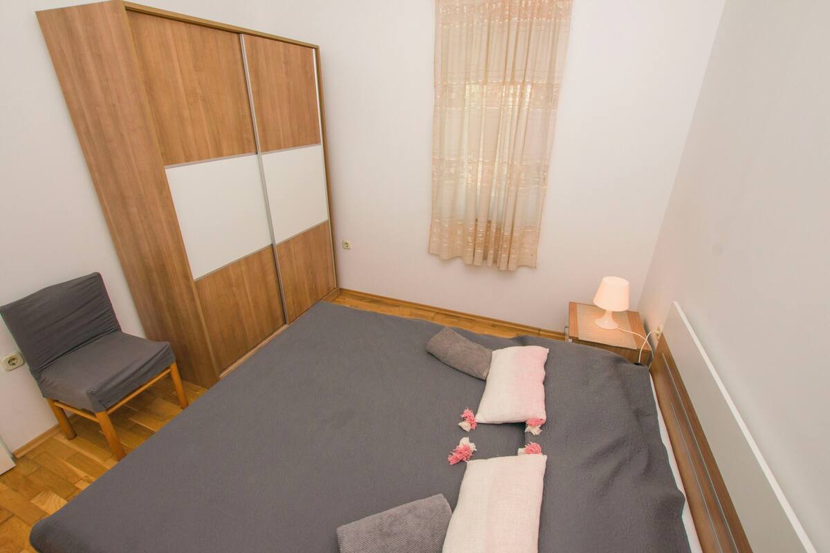 Une chambre à coucher comprenant un lit, une chaise, une table de chevet avec une lampe et une armoire en bois.