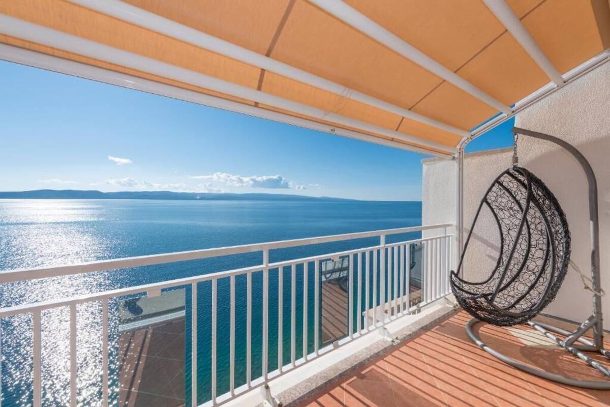 A balcony with a view of the sea, a hanging chair, and a railing.
