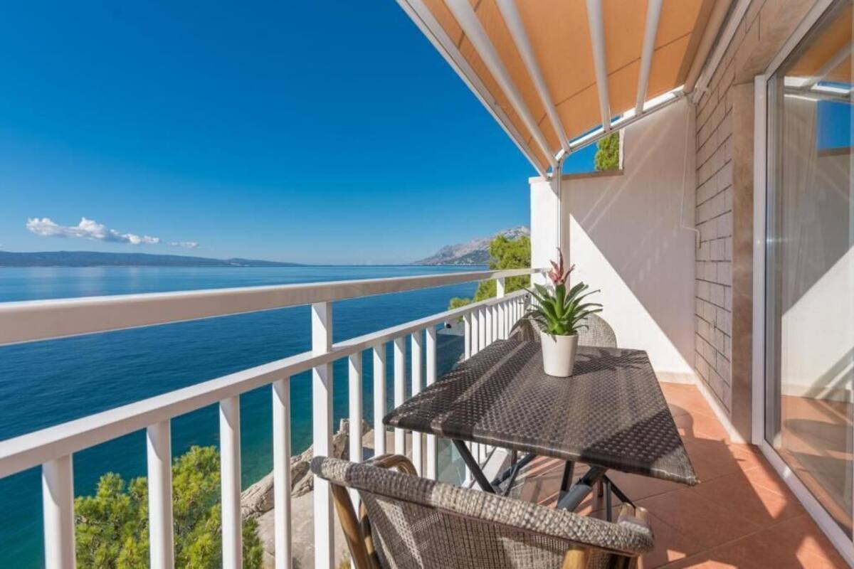 A balcony with a view of the sea, a table with a potted plant, and wicker furniture.