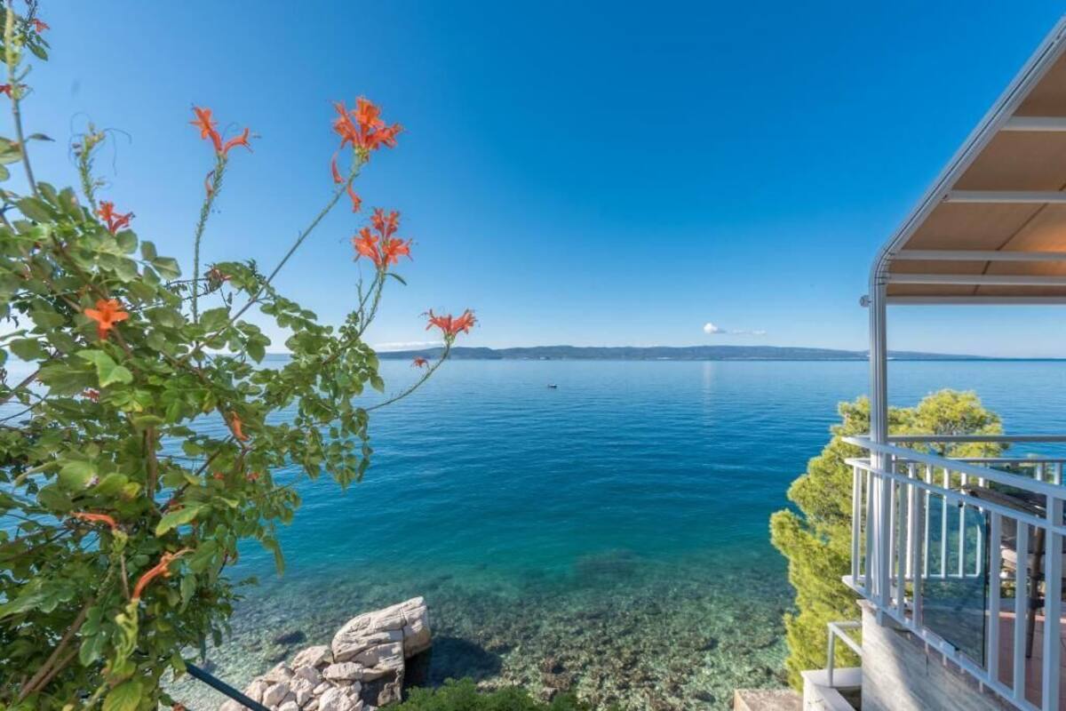 A clear view of a lake with a balcony overlooking the water, surrounded by greenery and a clear sky.