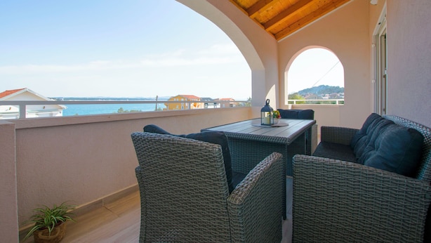 Un balcon agrémenté de meubles en osier, une table avec une bouteille, et une vue sur la mer.