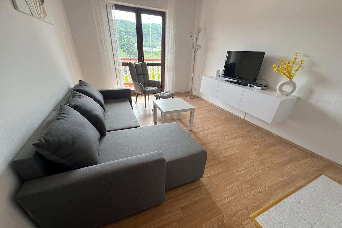 A modern living room with a grey sectional sofa, a small white table, and a TV on a white cabinet.
