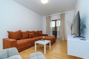 Ein Wohnzimmer mit einem braunen Sofa, einem weißen Couchtisch, einem grauen Sessel und einem Fernseher auf einem weißen Schrank.