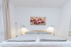 A bed with two pillows, a wall-mounted painting of flowers, and two bedside lamps. - Apartments Milan (Lopar)
