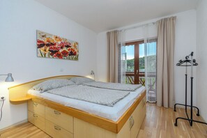 Et soveværelse med seng, senget lampe, et vindue med gardiner, et knagered og et billede på væggen.