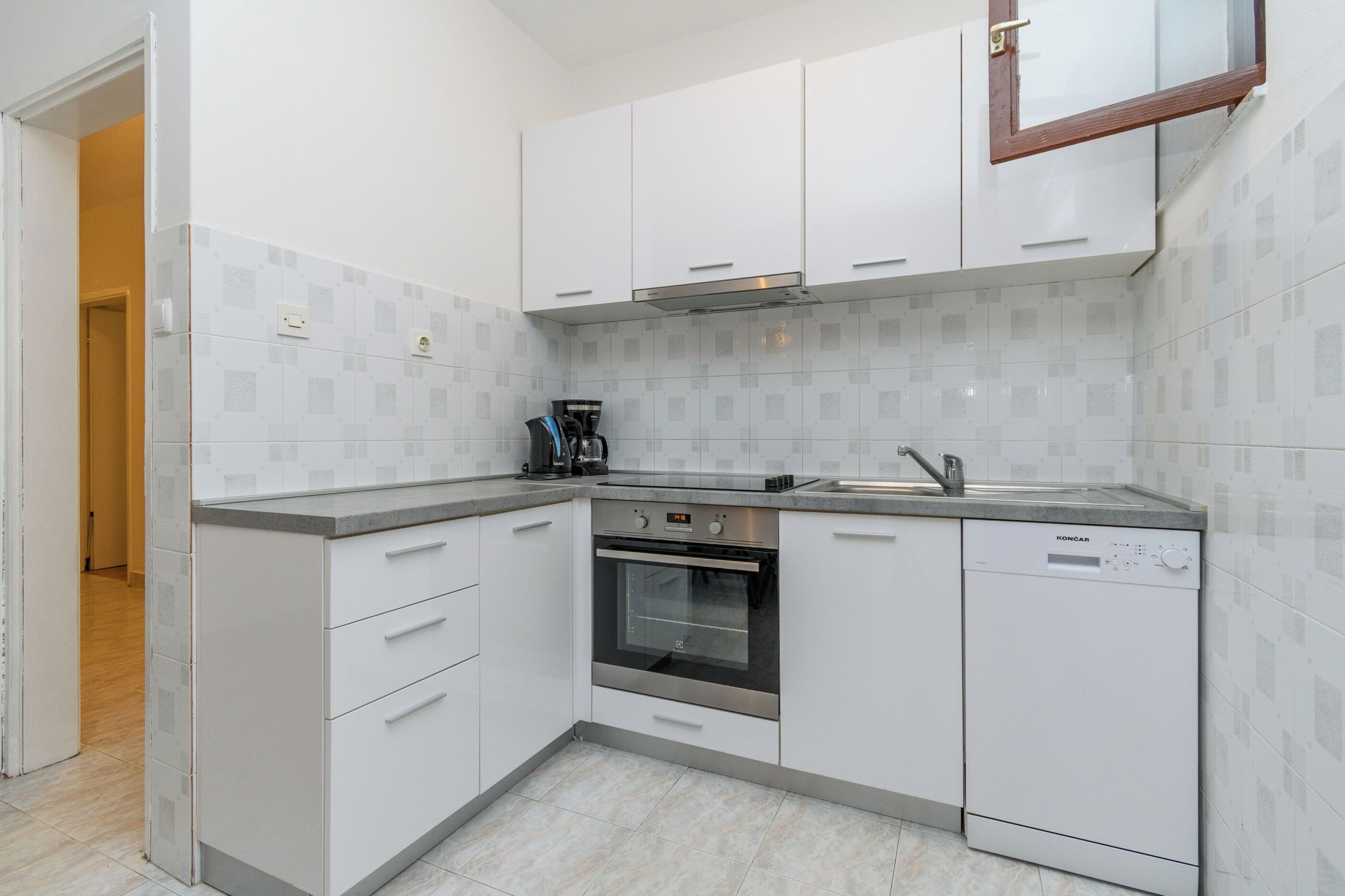 A modern kitchen with white cabinets, a built-in oven, a coffee maker, and a dishwasher.