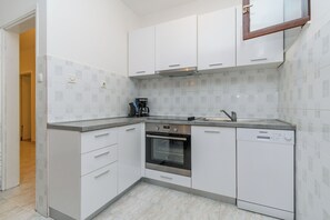 Une cuisine moderne avec des meubles blancs, un four encastré, une machine à café et un lave-vaisselle.