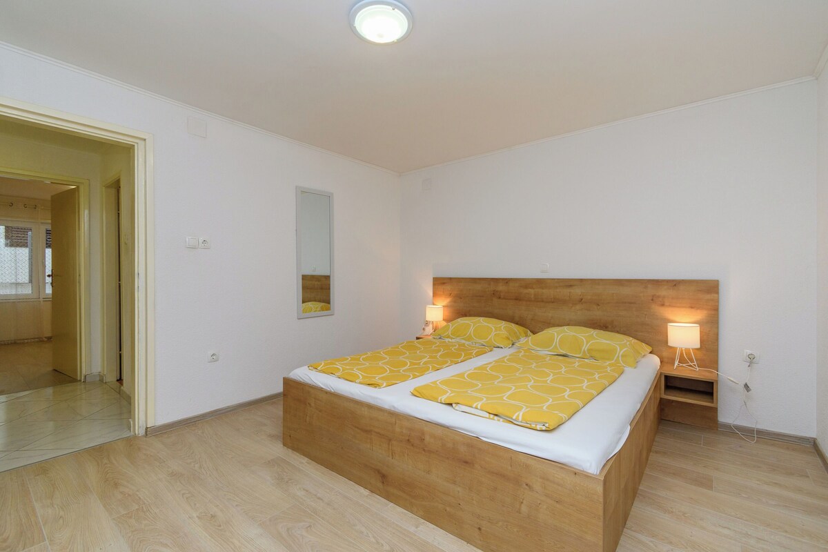 Ein Schlafzimmer mit einem hölzernen Bett, einem Spiegel, einer Nachttischlampe und einer Tür zu einem anderen Raum.