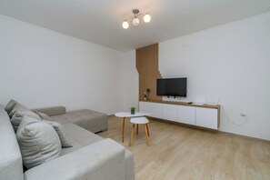 Un salon moderne avec un canapé gris, une petite table ronde et un téléviseur fixé sur un mur recouvert de panneaux en bois.