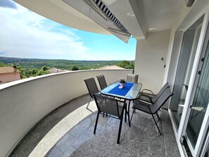 En balkon med et bord og stole, en potteplante og udsigt over et grønt landskab.