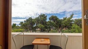 Un balcon avec deux chaises, une petite table et un verre. Le balcon offre une vue sur les arbres et les bâtiments environnants.