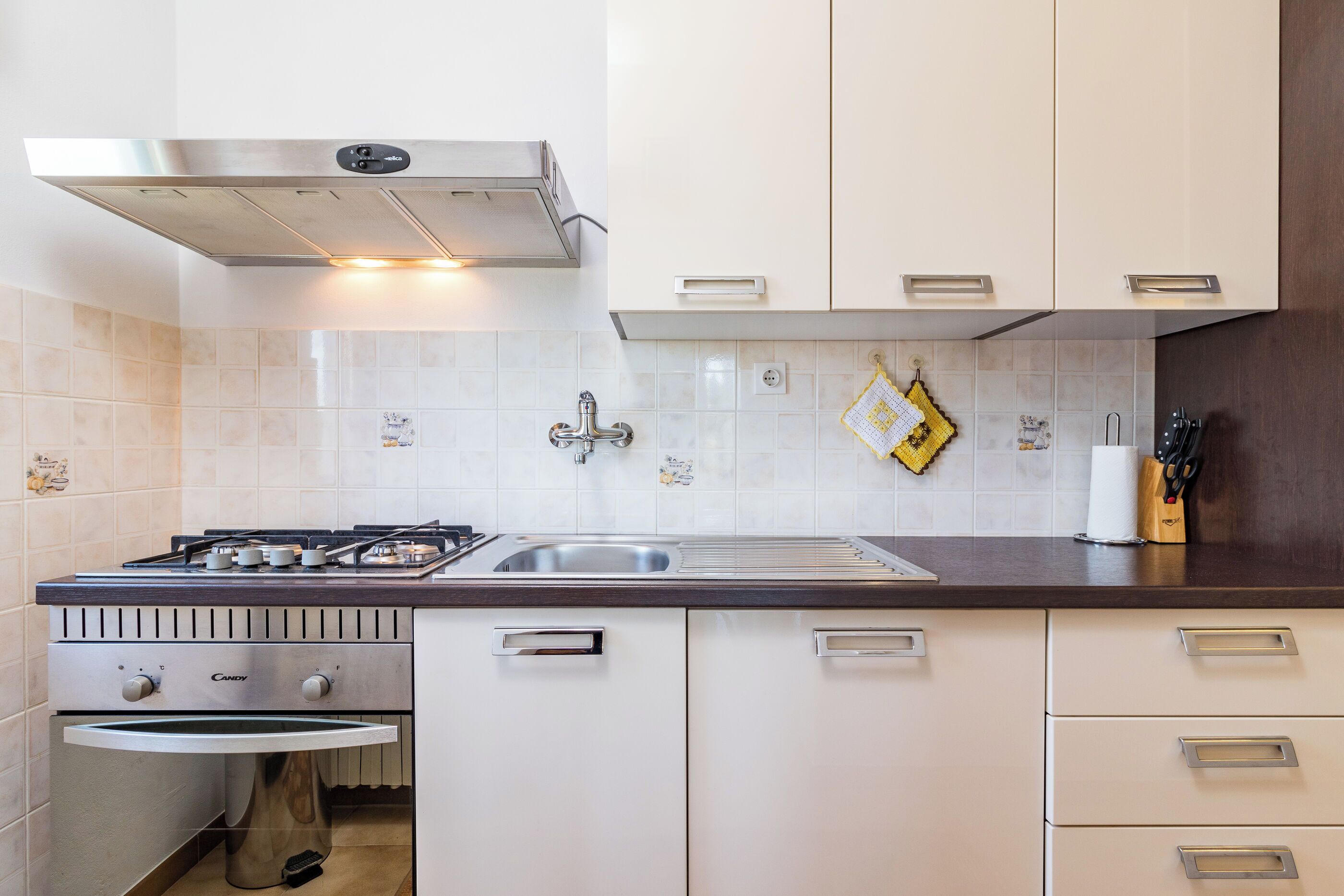A modern kitchen with a gas stove, stainless steel sink, white cabinets, and a range hood.