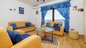 A living room with two yellow sofas, a glass coffee table, and a view of the sea through blue curtains. - Apartment Lea (Crikvenica)