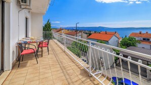 A balcony with a table and chairs, overlooking a coastal town and sea. - Apartment Lea (Crikvenica)