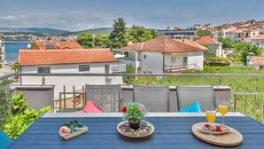 A terrace with a table set for a meal, overlooking a coastal town with red-roofed houses and a clear sky. - Apartments Piveta (Okrug)