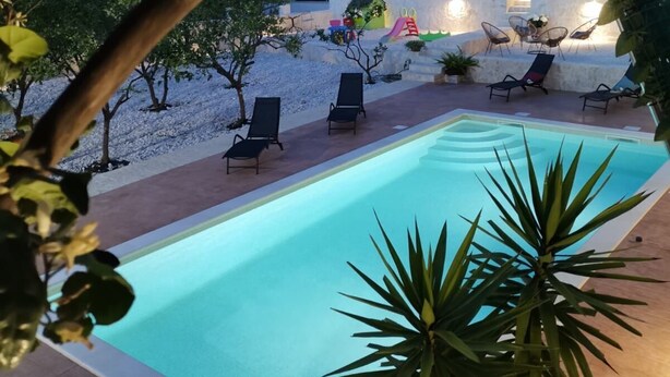 A swimming pool with lounge chairs, a small garden area, and a building in the background. - Apartments Piveta (Okrug)