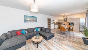 A modern living room with a sectional sofa, a coffee table, and a dining area with a table and chairs. - Apartments Piveta (Okrug)
