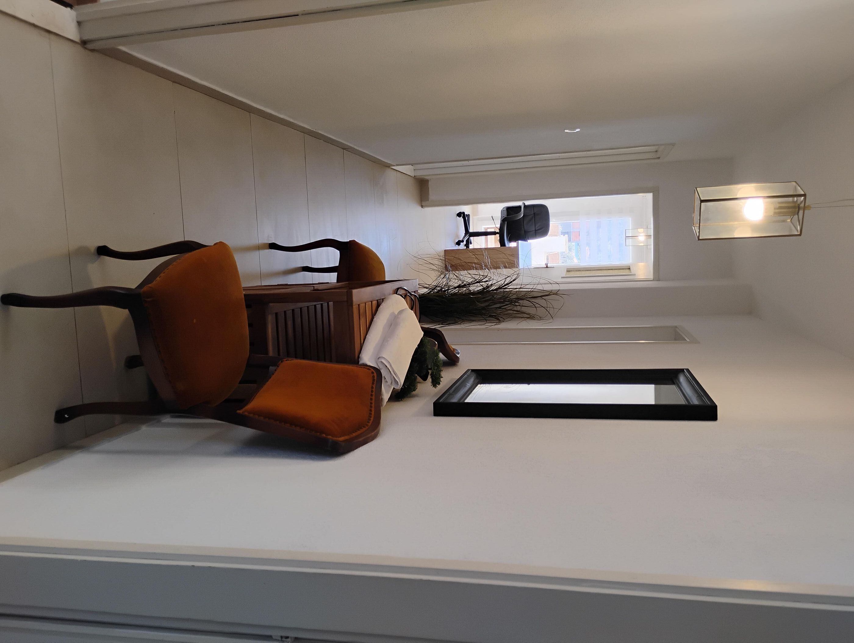 A modern room with a white wall, a wooden chair, a small table, and a window with a view.