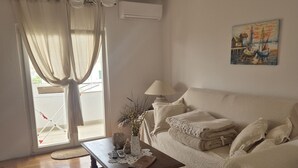 A cozy room with a sofa, a coffee table with a vase and a remote control, a lamp, and a painting on the wall. - Apartment Anea (Marina)