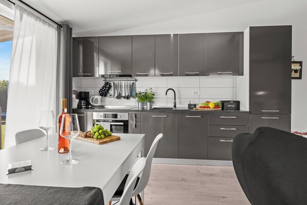 Une cuisine moderne avec des meubles gris, des appareils en acier inoxydable et un coin repas comprenant une table et des chaises.