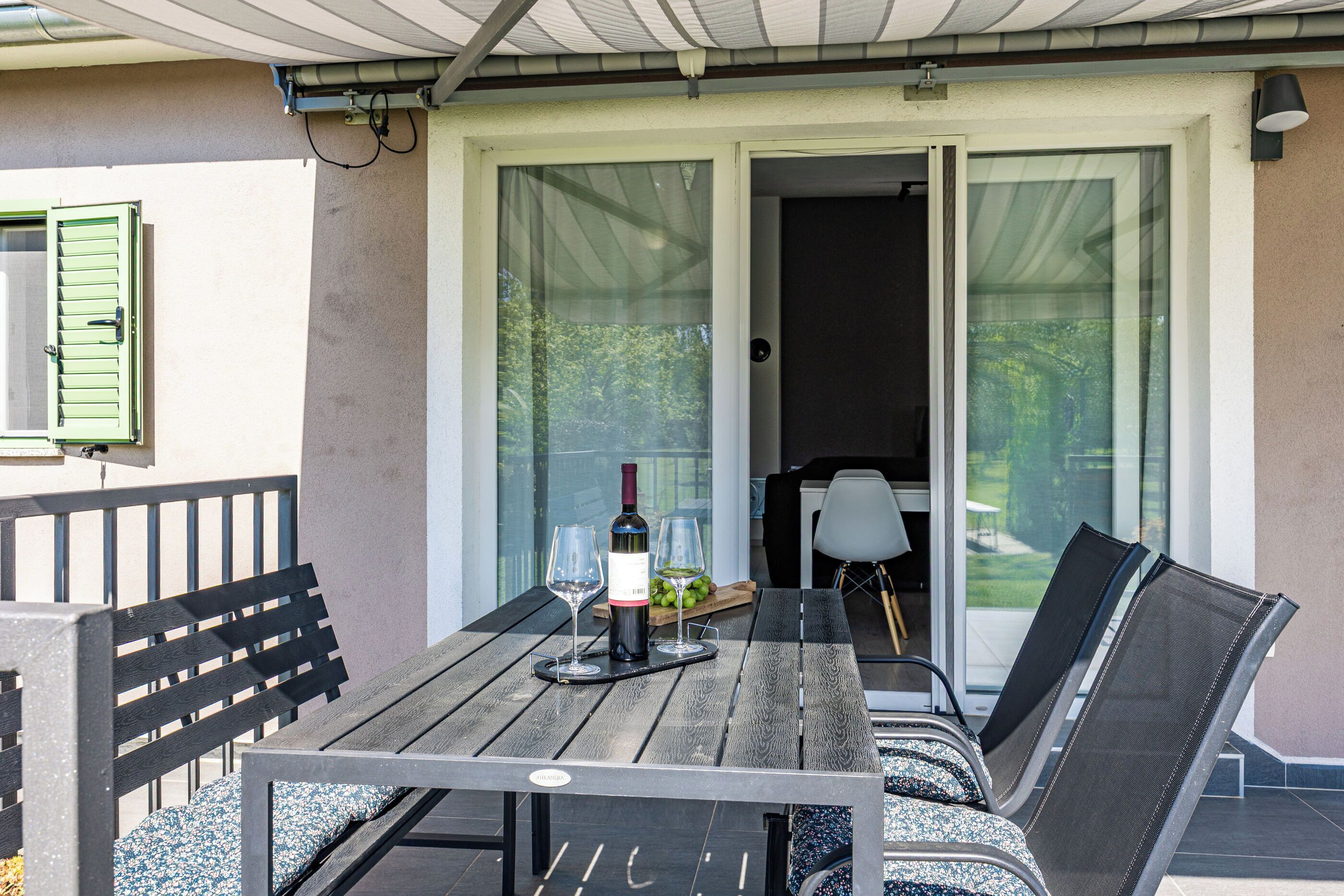 An outdoor patio with a table, chairs, and a bottle of wine.