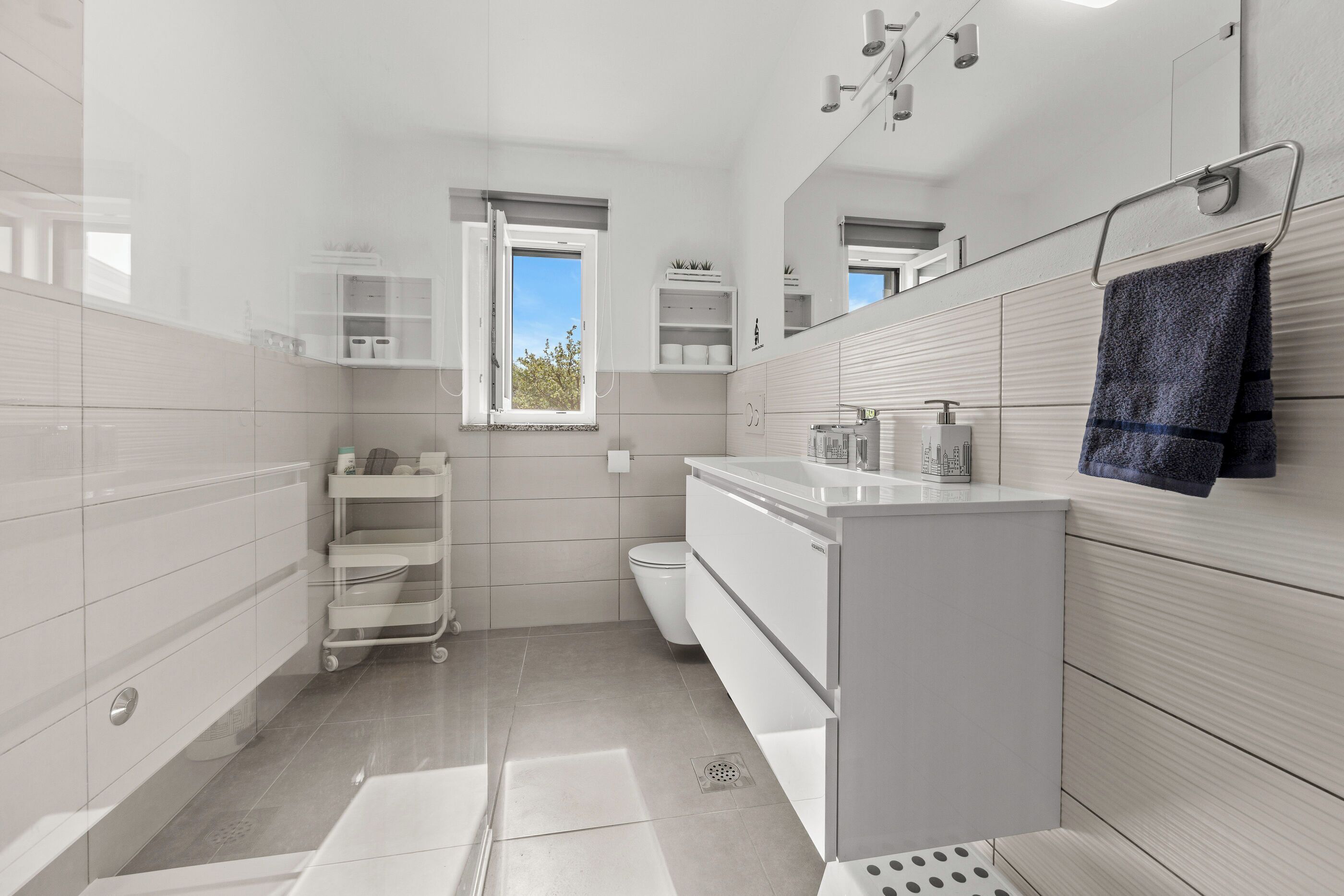 Een moderne badkamer met witte kastjes, een ingebouwd raam en een handdoekrek.