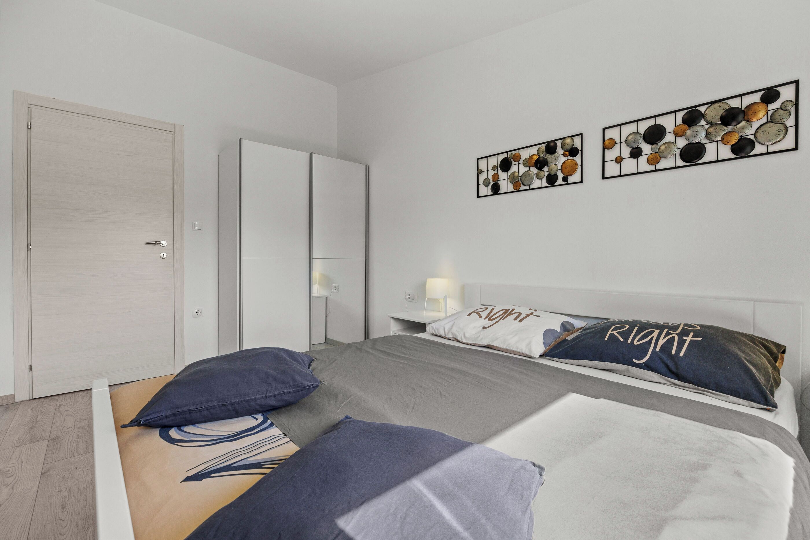 A modern bedroom with a bed, two pillows, a nightstand, and wall art.