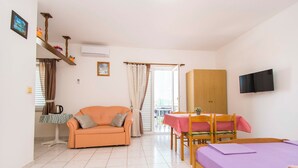 A room with a sofa, a dining table with chairs, a bed, a TV mounted on the wall, and a door leading to an outdoor area. - Apartments Nada (Murter-Kornati)