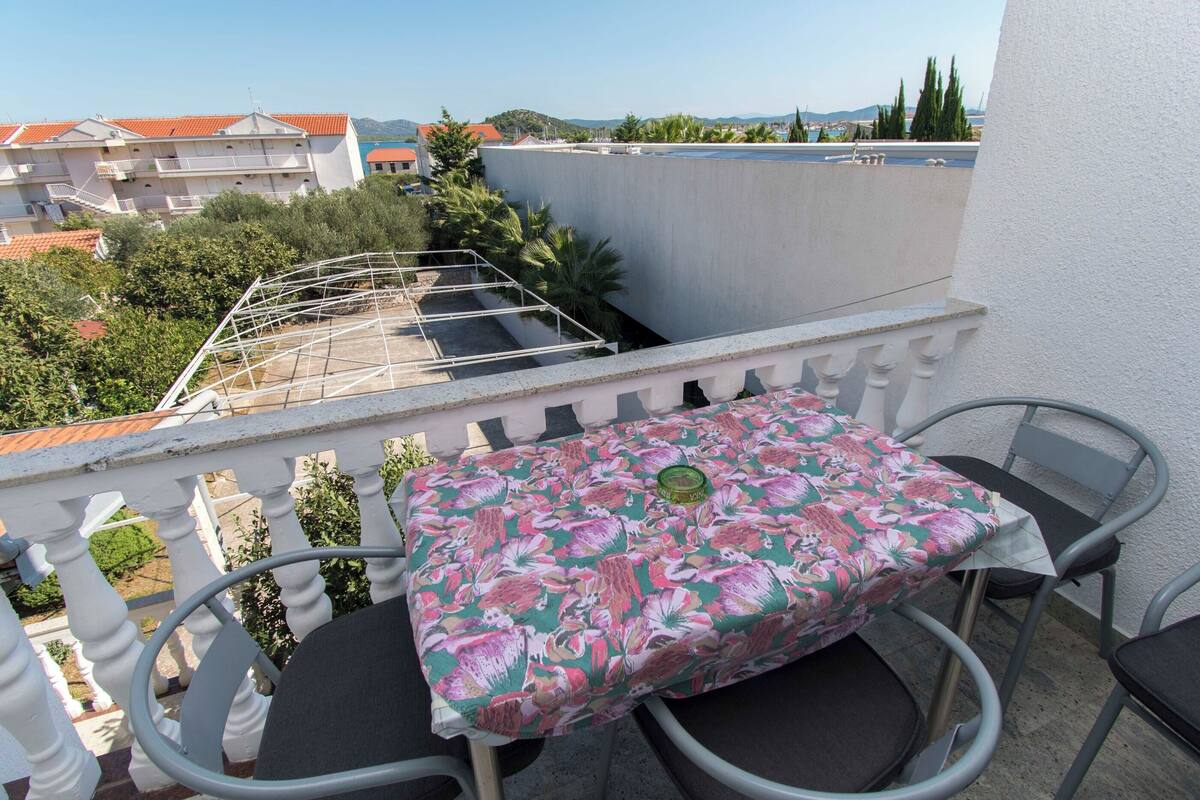 A balcony with a table and chairs, overlooking a garden and buildings.