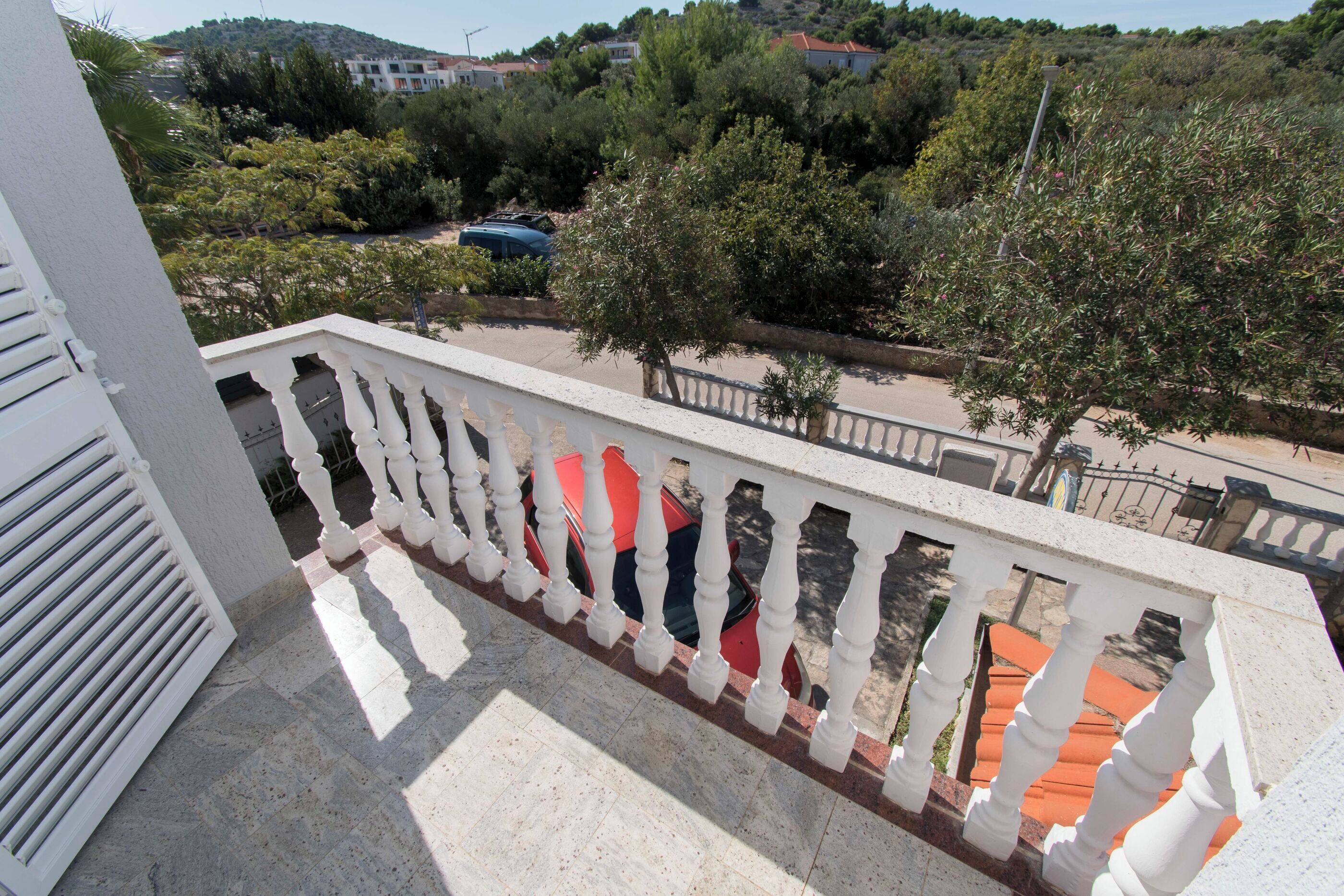 A balcony with white balustrades overlooking a residential area with trees and parked cars.