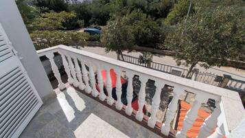 A balcony with white balustrades overlooking a residential area with trees and parked cars.
