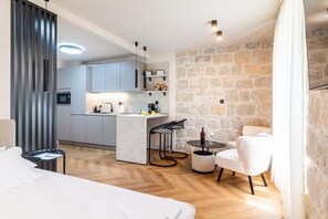 A modern hotel room with a kitchenette, a dining area with a small table and chairs, and a large bed. - Apartments Centre In Stone House (Split)