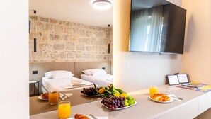 A hotel room with a stone wall, a flat-screen TV, a breakfast table with croissants, fruit, and orange juice. - Apartments Centre In Stone House (Split)