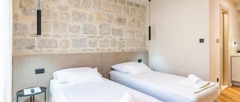 A hotel room with two single beds, a stone wall, a small table, and a door leading to a bathroom.